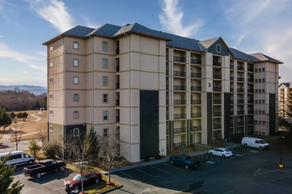 A wide shot of the Hawks Nest's 5-story building with a spacious parking lot and a scenic landscape in the background. The image suggests a welcoming, resort-style environment with room for groups and families.