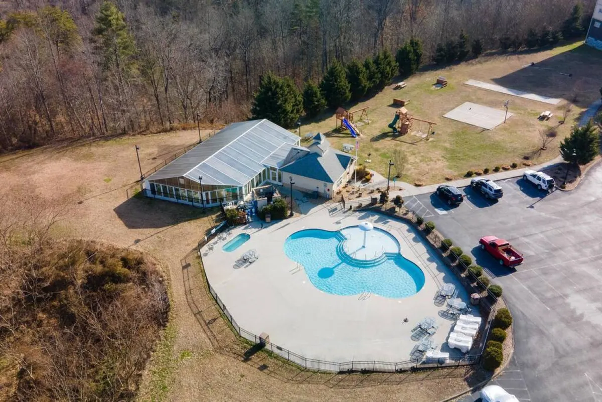 This exterior image showcases a vibrant outdoor swimming pool with a recreational building and colorful playground equipment nearby. The scene is lively with ample space for children to play and families to gather, with the pool and playground as focal points.