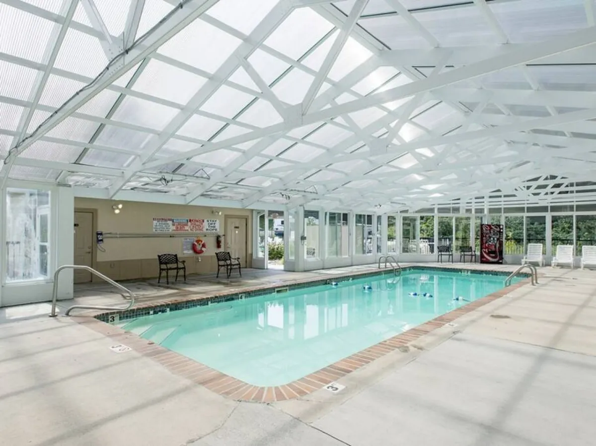 The interior shot features a modern, spacious indoor swimming pool with a transparent ceiling letting in natural light. Surrounding seating invites relaxation and socializing, making it ideal for year-round enjoyment.