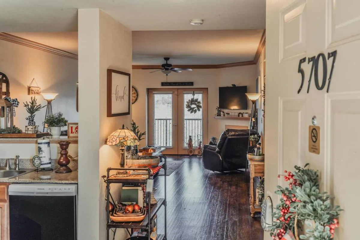 A kitchen counter with tasteful decor opens to a cozy living room seating area, with balcony doors letting in abundant natural light. The kitchen and living area are visually connected, making it easy for guests to gather and converse while preparing meals or relaxing.