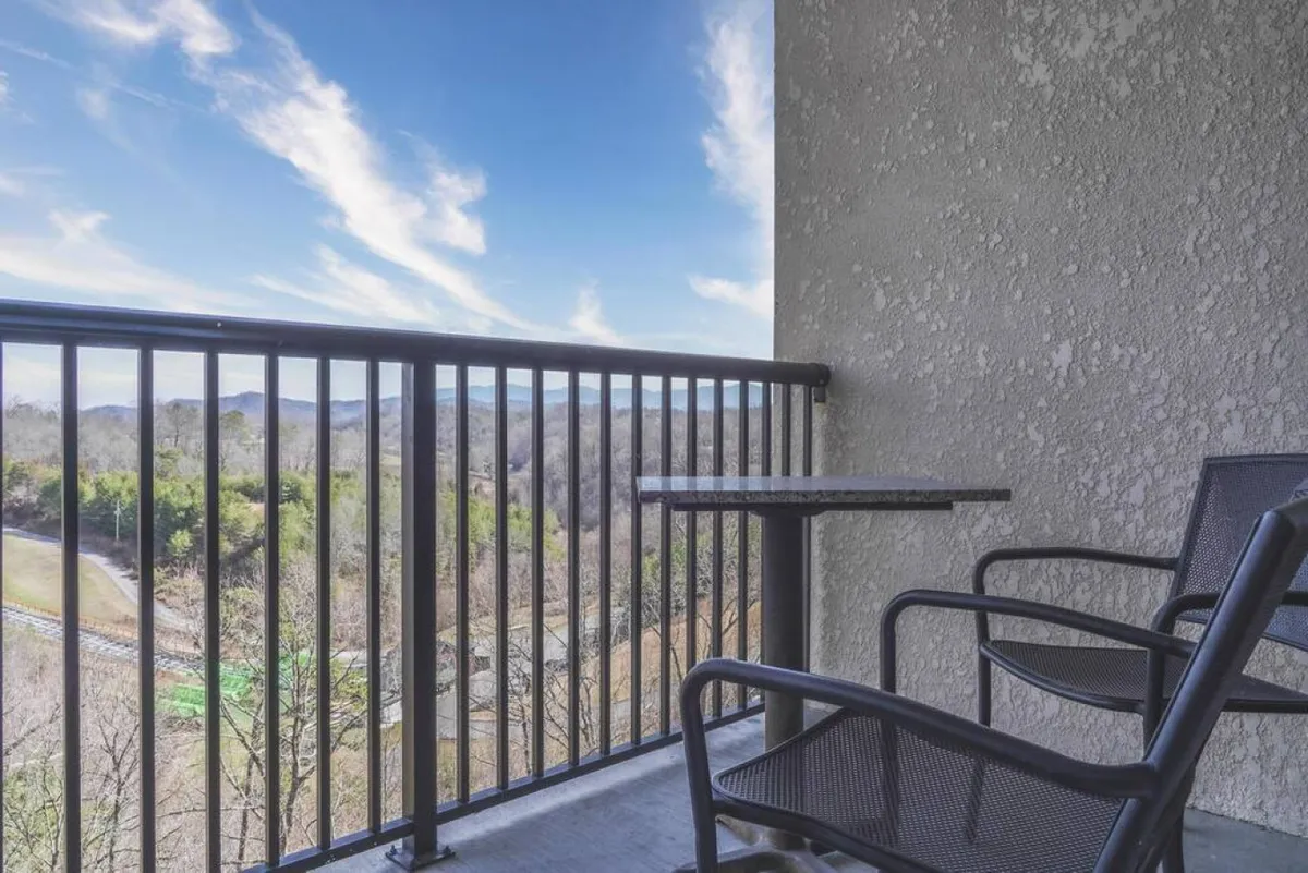 A balcony with a table and chairs overlooks a spectacular mountain view. The scene suggests enjoying coffee or sharing stories while admiring the natural beauty just outside the living space, reinforcing the connection between indoors and the surrounding landscape.
