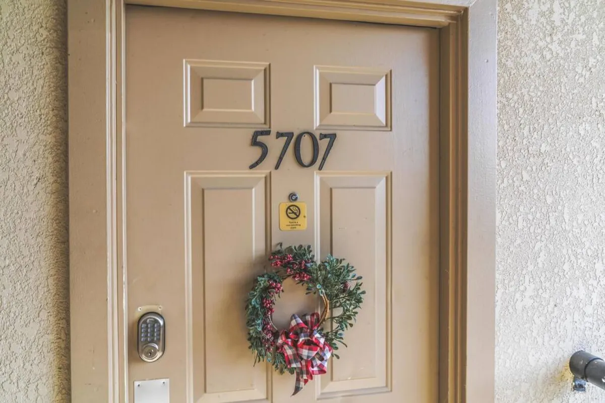 A close-up of a unit's entry door with an inviting wreath and a clear view of the door number and accessible lock mechanism. The clean, wide entryway offers a visual cue of easy, step-free accessibility.
