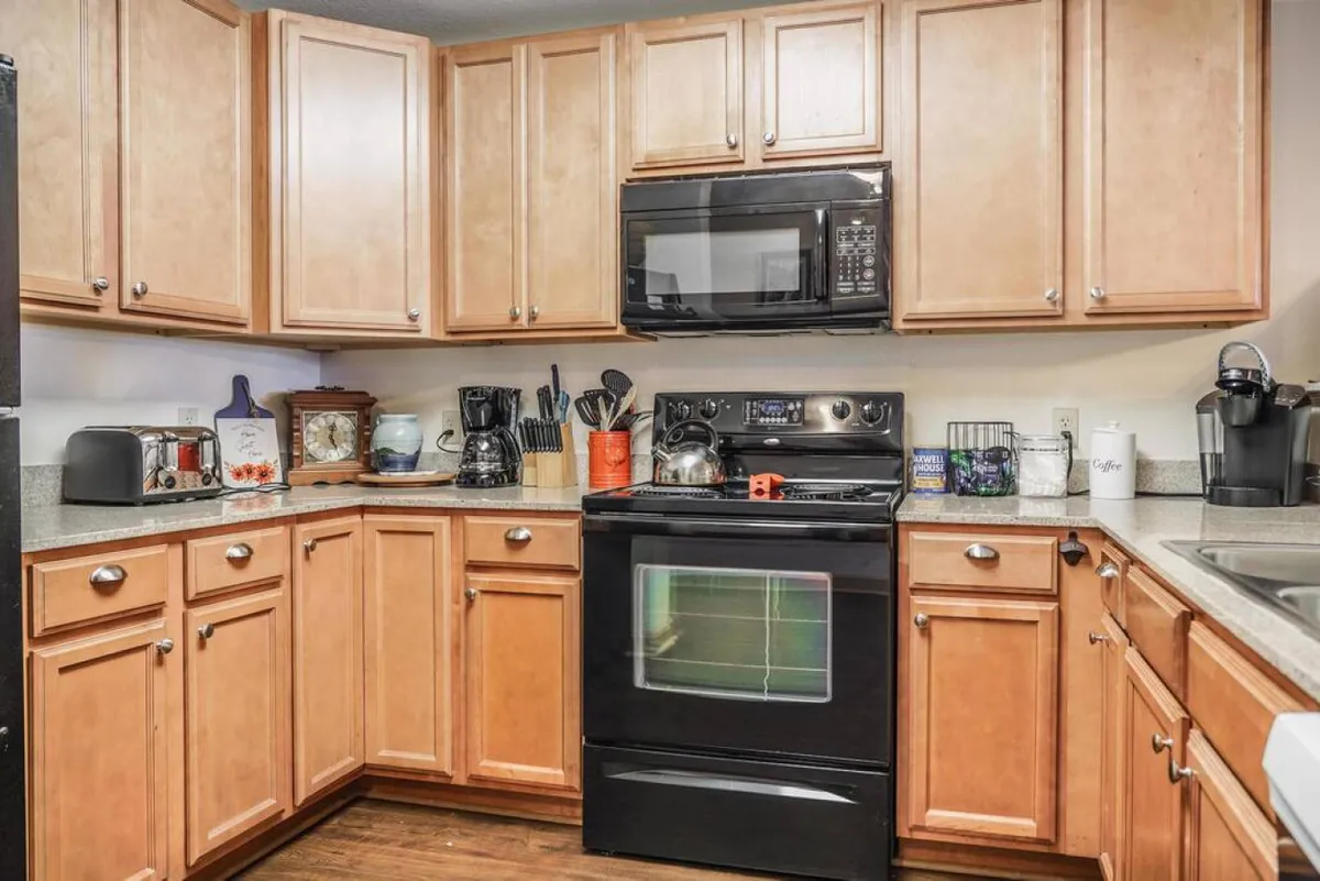 A warm, well-equipped kitchen featuring stainless steel appliances, wooden cabinets, and a coffee maker on the counter. The space is brightened by natural and ambient light, emphasizing both functionality and comfort for long or short stays.