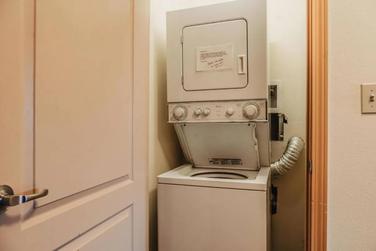 A stacked washer and dryer unit, neatly tucked into a dedicated laundry area with a helpful note on the dryer. The space feels clean and practical, underscoring the convenience of in-unit amenities for guests staying longer.