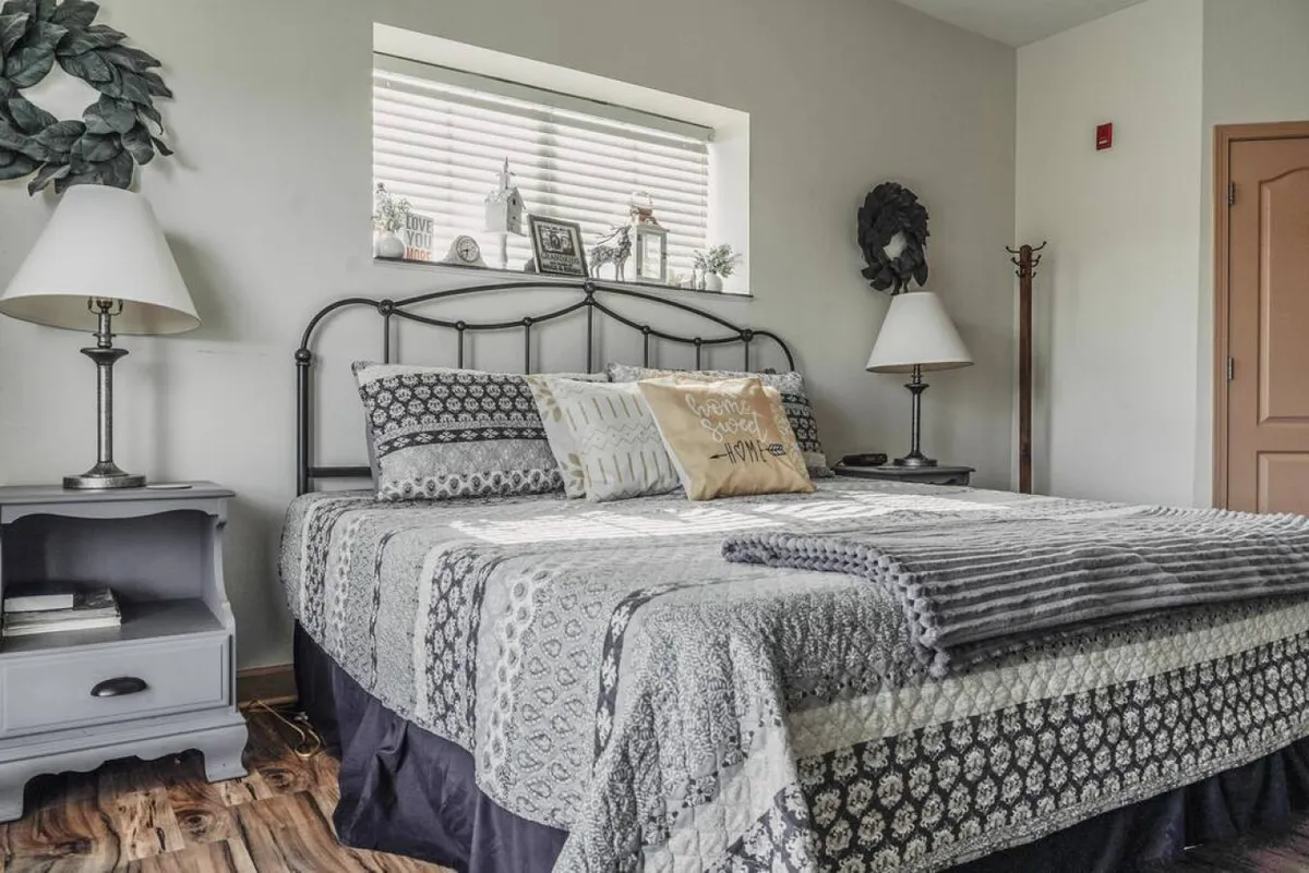 The image showcases a serene bedroom featuring a comfortable bed adorned with decorative pillows and warm blankets. Natural light streams in through a window with tasteful decorations, creating an inviting and peaceful atmosphere ideal for relaxation.