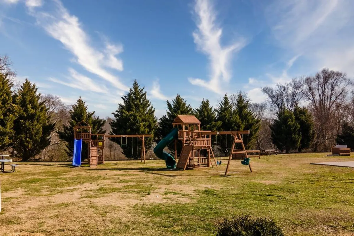 A cheerful exterior scene of a playground with a slide, swings, and lush greenery. The space is designed for children’s play and family gatherings, inviting both energetic play and social relaxation.